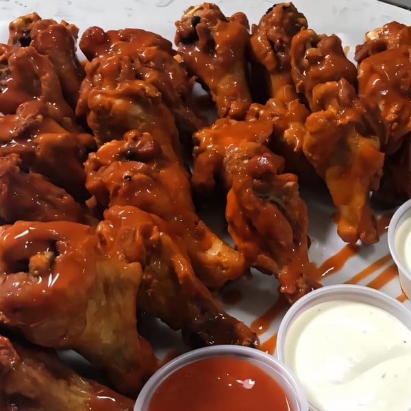 Kraving Kebab Pizza's buffalo wings, coated in shiny orange sauce, served with dipping sauces.