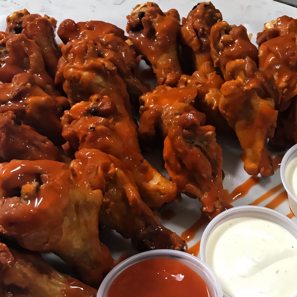 Kraving Kebab Pizza's buffalo wings, coated in shiny orange sauce, served with dipping sauces.