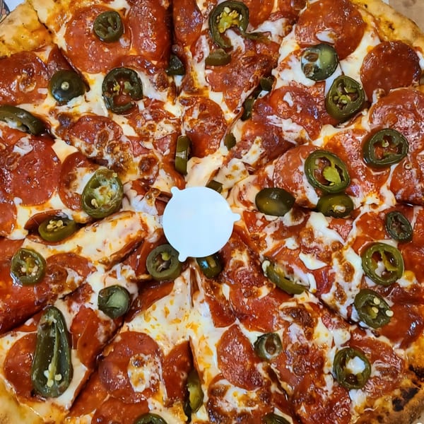 A Kraving Kebab Pizza with pepperoni, jalapeños, and melted cheese, sliced and ready to eat.