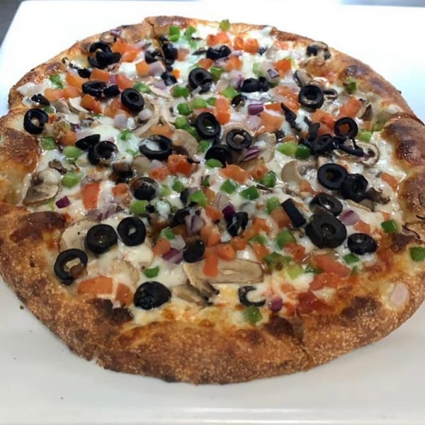 Kraving Kebab Pizza's vegetarian pizza with olives, mushrooms, peppers, and onions on a white plate.