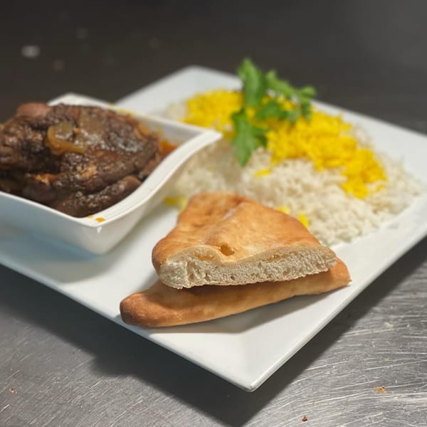 A white plate with a bowl of stew, white rice with yellow saffron, and flatbread.