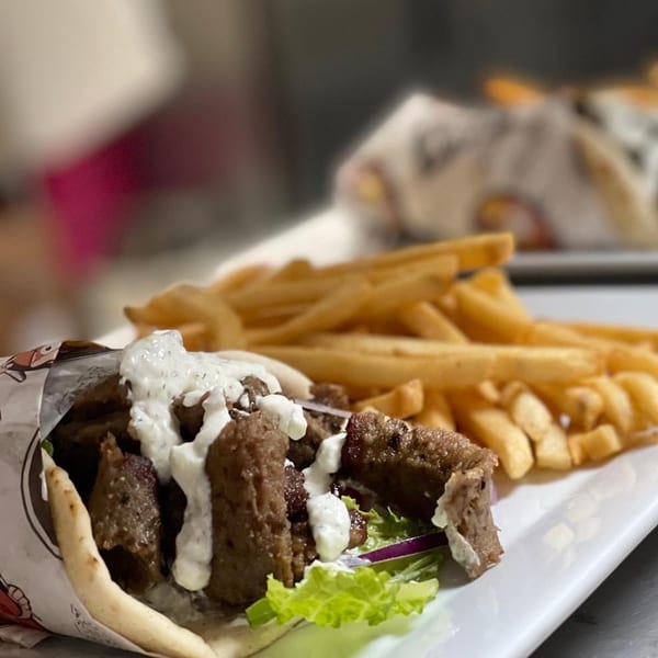 A Kraving Kebab gyro with meat, lettuce, onions, and white sauce, served with french fries.